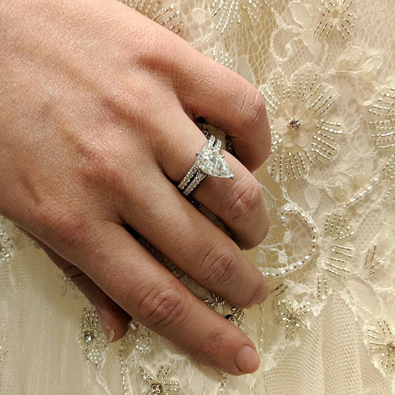 Woman's hand wearing a custom engagement ring and wedding band over a wedding dress